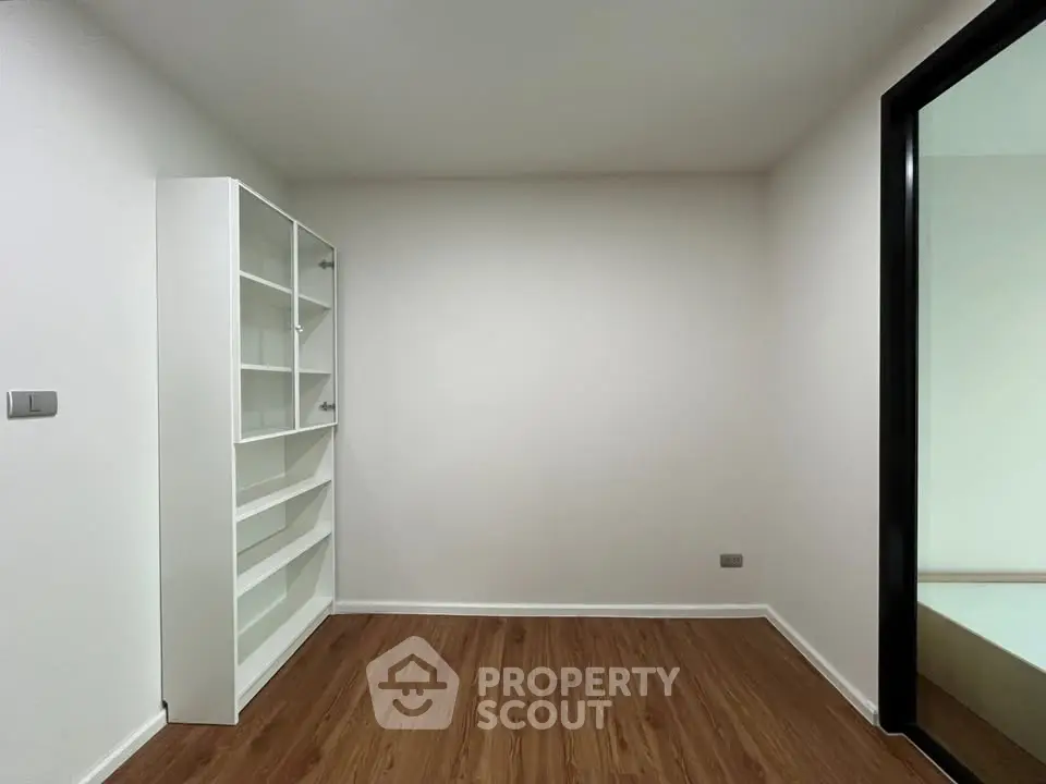 Minimalist room with wooden flooring and white shelving unit, perfect for a cozy study or storage space.