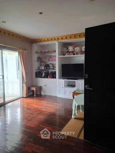 Charming living room with built-in shelves and plush toys, featuring elegant wooden flooring and natural light.