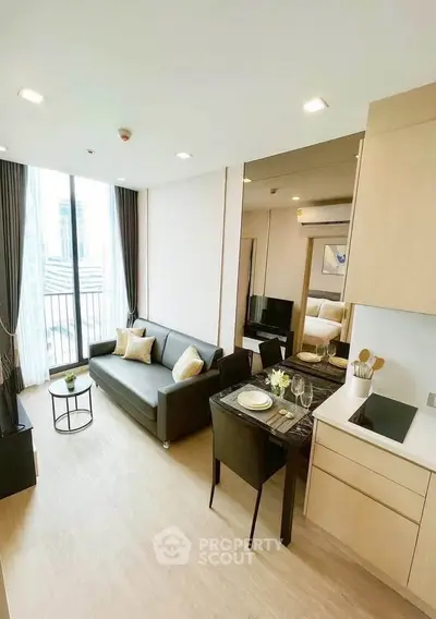 Modern open-plan living room with kitchen in stylish apartment, featuring sleek furniture and large windows.