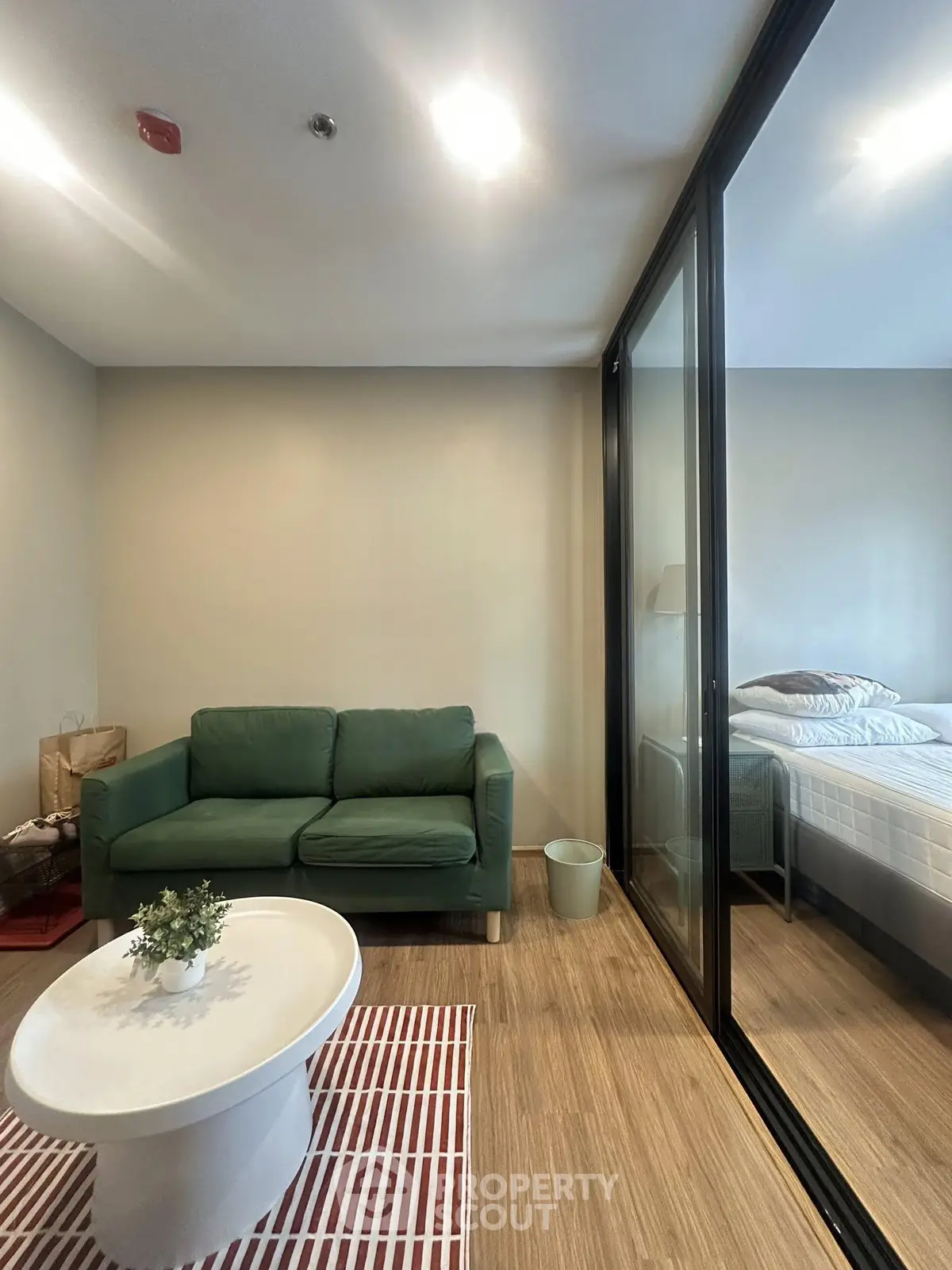 Modern living room with green sofa and glass partition leading to bedroom
