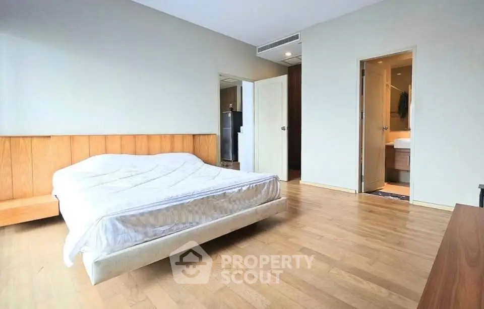 Spacious bedroom with wooden flooring and ensuite bathroom in modern apartment.