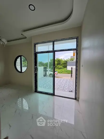 Modern room with large glass doors opening to a patio, featuring sleek marble flooring and a circular window.