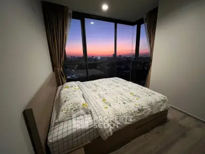Cozy bedroom with stunning sunset view through large windows, featuring modern decor and wooden flooring.