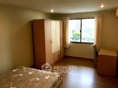 Spacious bedroom with wooden flooring and large window offering city view