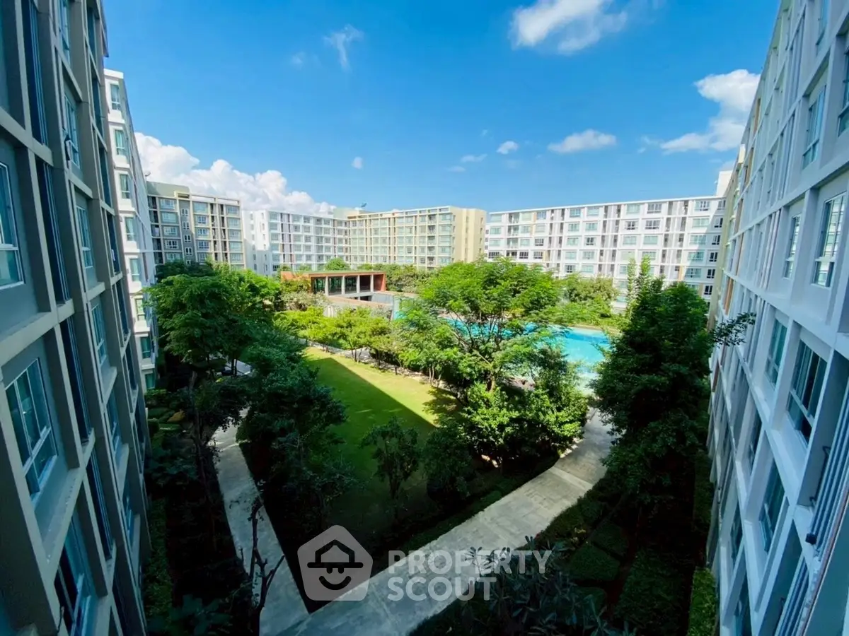 Stunning view of modern apartment complex with lush garden and pool area under clear blue sky.