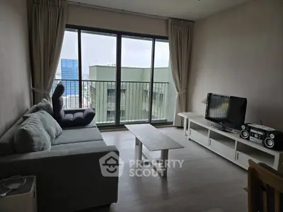 Modern living room with large windows and city view, featuring a cozy sofa and entertainment center.