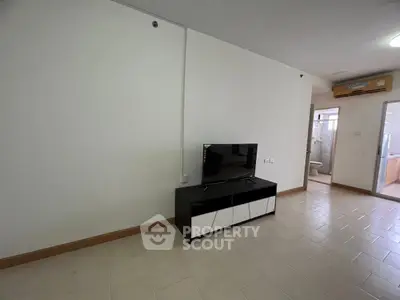 Modern living room with sleek TV stand and tiled flooring, adjacent to bathroom and kitchen.