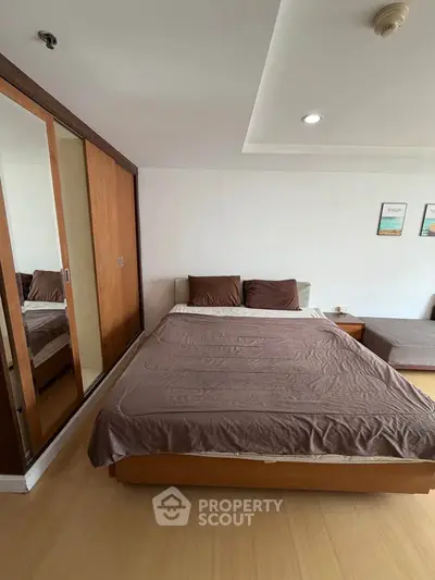 Spacious bedroom with wooden flooring and mirrored closet doors in modern apartment.