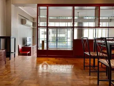 Spacious living room with wooden flooring and modern furniture, featuring a large window for natural light.