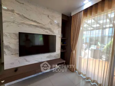 Modern living room with marble accent wall and large TV, featuring elegant curtains and natural light.