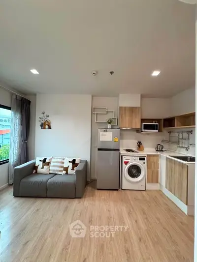 Modern living room with integrated kitchen, featuring sleek appliances and cozy seating area.