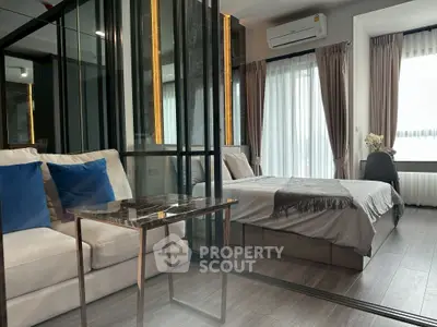 Modern bedroom with glass partition and cozy seating area, featuring elegant decor and natural light.