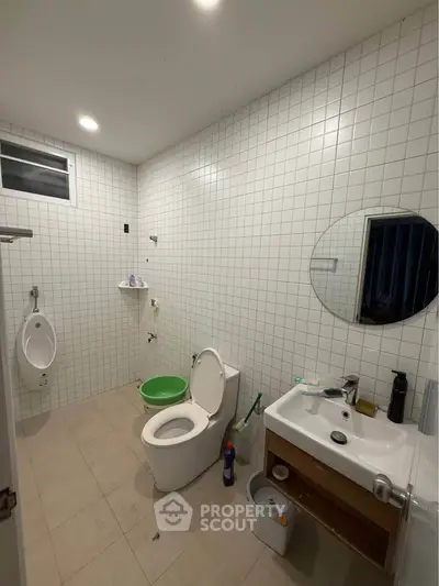 Spacious bathroom with modern fixtures and tiled walls, featuring a urinal and round mirror.