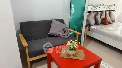Cozy living area with modern sofa and vibrant red table, adjacent to a stylish bedroom.