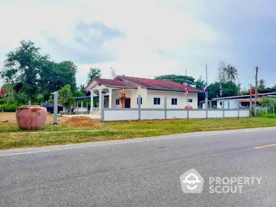 Charming single-story house with red roof and spacious yard near the road in a serene neighborhood.