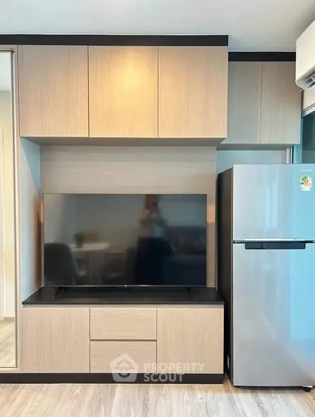 Modern living room with sleek cabinetry and large flat-screen TV, adjacent to a stainless steel refrigerator.