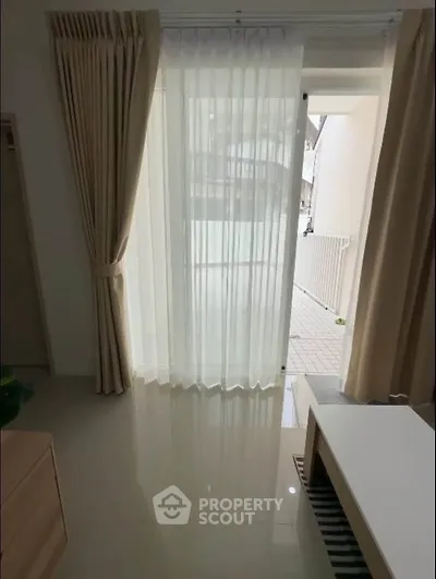 Bright living room with floor-to-ceiling windows and elegant curtains, offering a glimpse of the outdoor area.