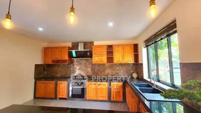 Spacious kitchen with wooden cabinets and modern appliances, featuring large windows and stylish lighting.