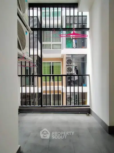 Modern apartment balcony with air conditioning units and clothes hangers, offering a view of neighboring buildings.