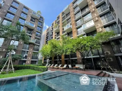 Luxurious modern condominium complex with a serene pool area surrounded by lush greenery and stylish lounging spaces, offering a tranquil urban oasis.