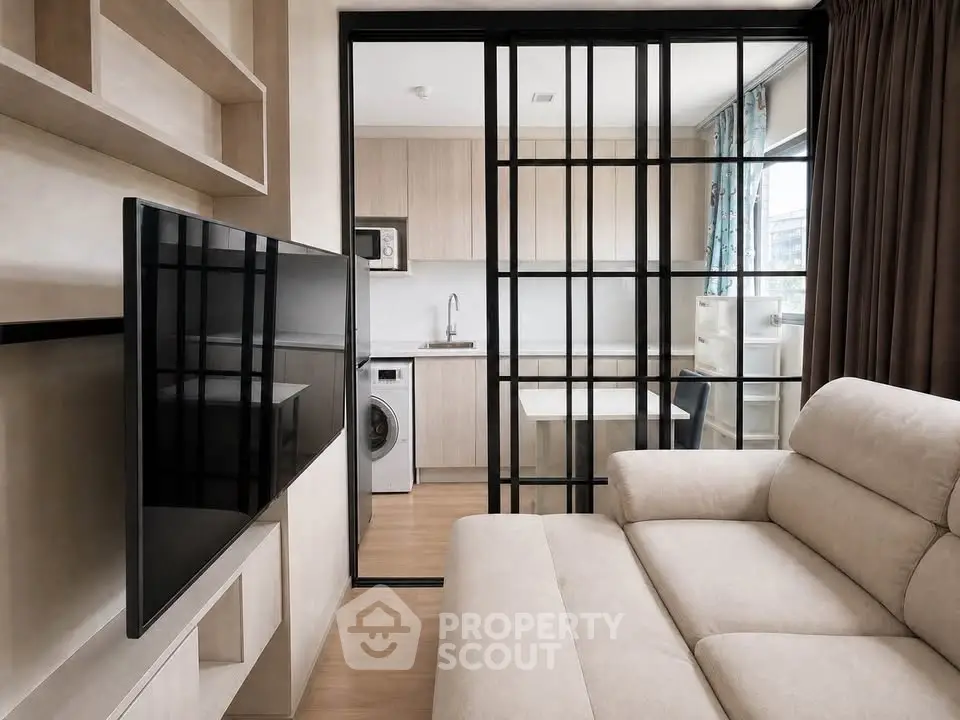Modern living room with sliding glass doors leading to a compact kitchen featuring a washing machine.