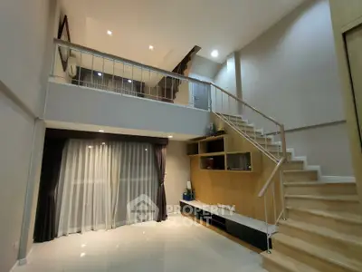 Spacious modern living room with high ceiling and mezzanine, featuring elegant staircase and large windows.