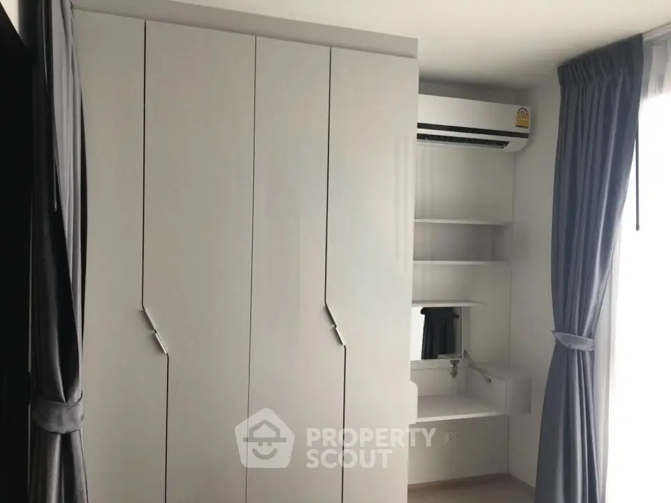Modern bedroom with sleek wardrobe and air conditioning unit, featuring natural light from large window.