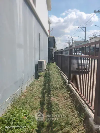 Charming narrow garden pathway alongside a modern residential building, offering a private outdoor space with potential for landscaping.