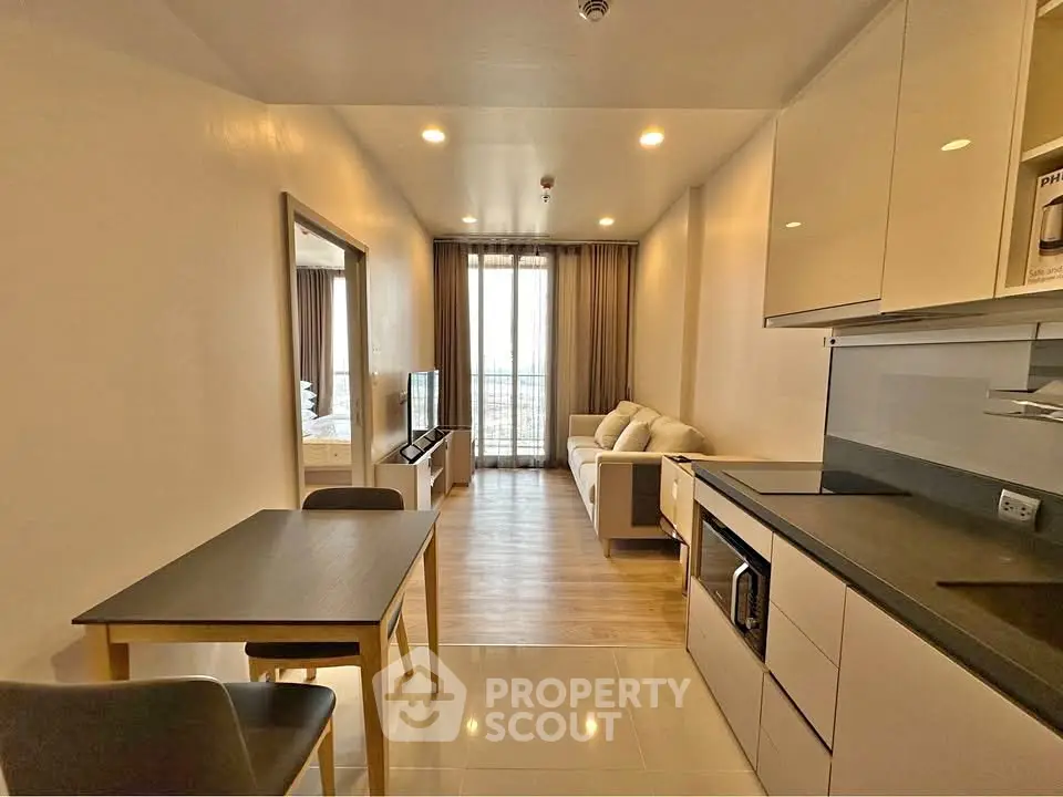 Modern open-plan living room with sleek kitchen and cozy seating area, featuring a large window for natural light.