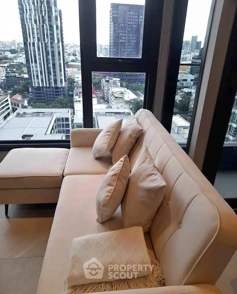 Modern living room with city view from high-rise apartment, featuring stylish beige sofa and large windows.