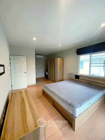 Spacious bedroom with modern wooden furniture and large window for natural light.