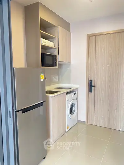 Modern compact kitchen with washing machine and fridge in sleek apartment.