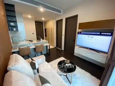 Modern living room with open kitchen, stylish decor, and large TV in a cozy apartment setting.