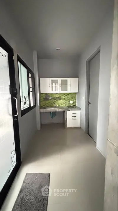 Compact kitchen with green backsplash and white cabinets in modern apartment