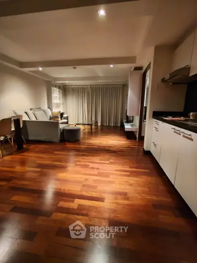 Spacious open-layout living room with wooden flooring and modern kitchen.