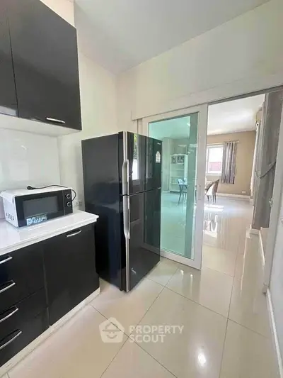 Modern kitchen with sleek black fridge and microwave, featuring glossy cabinets and sliding glass door.