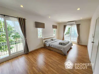 Spacious bedroom with balcony and large windows, featuring elegant wooden flooring and modern decor.