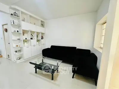 Modern living room with sleek black sofa and glass coffee table, featuring built-in white shelving.