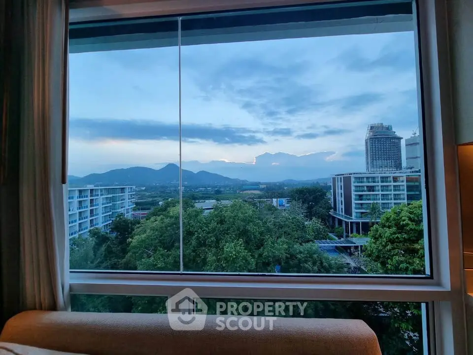 Stunning cityscape view from a high-rise window with lush greenery and mountains.