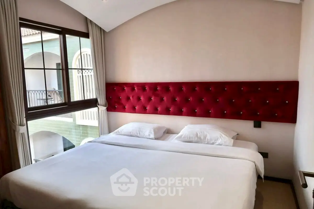 Elegant bedroom with plush red headboard and large window offering courtyard view.