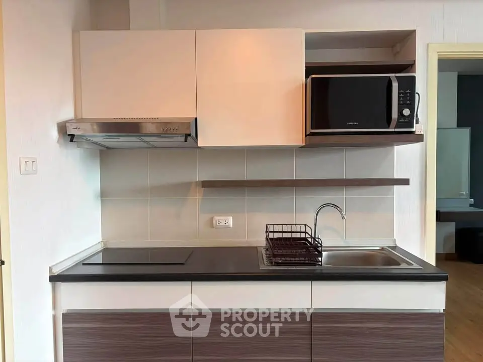 Modern kitchen with sleek cabinetry and built-in microwave, featuring an electric cooktop and stainless steel sink.