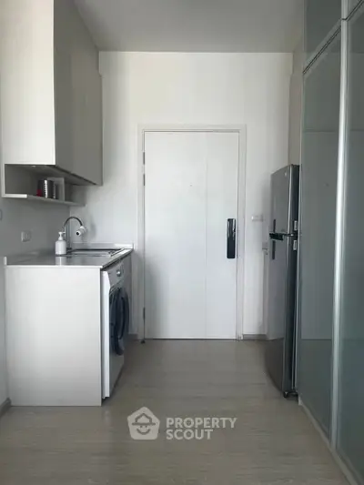 Modern kitchen with sleek appliances and minimalist design, featuring a washing machine and fridge.