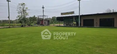 Spacious green field with adjacent building, perfect for sports or recreational activities.