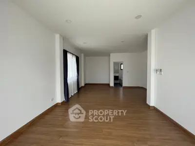 Spacious empty room with wooden flooring and large window, ideal for customization.