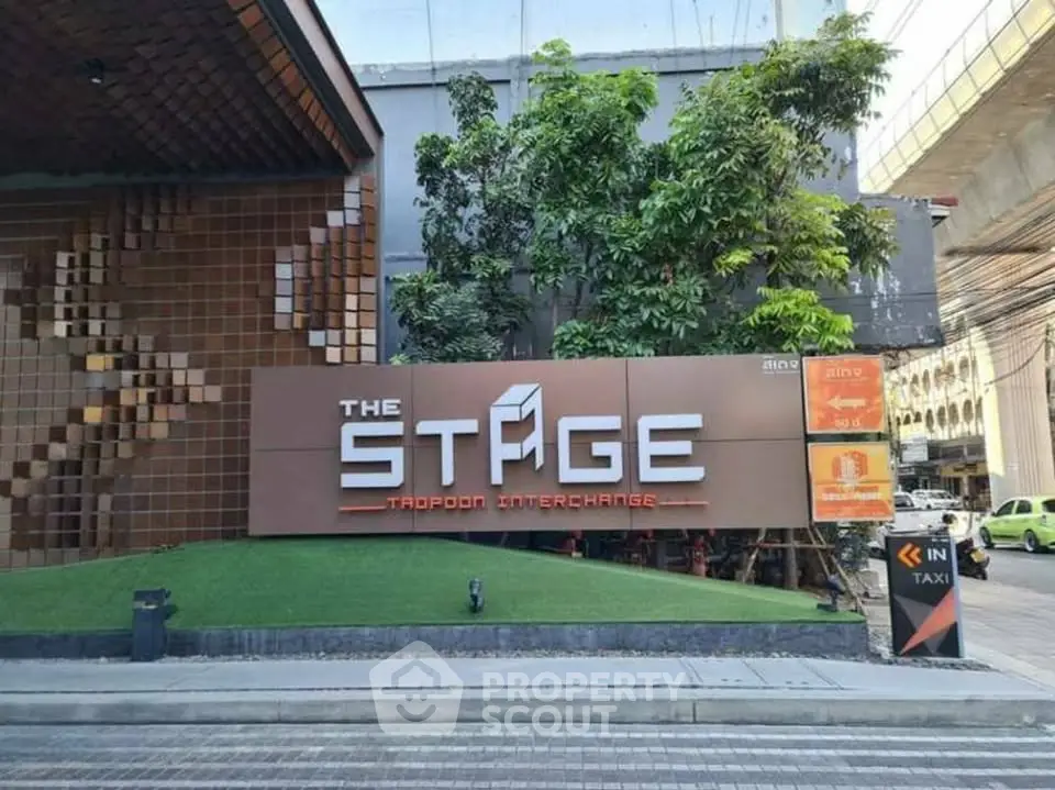 Modern building entrance with stylish signage at The Stage Taopoon Interchange, featuring lush greenery.