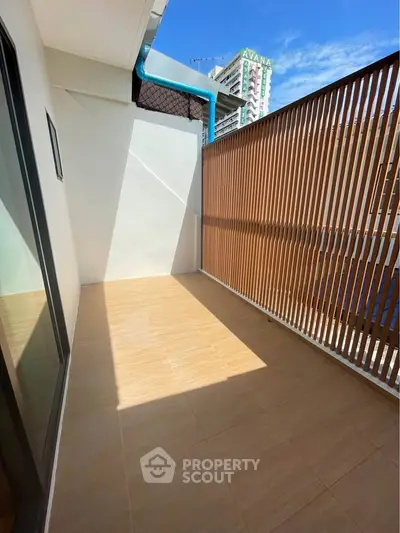 Spacious balcony with modern wooden slat privacy screen and city view, perfect for relaxation.