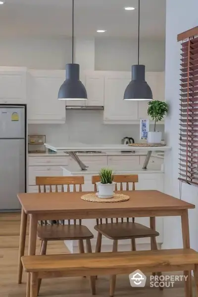 Modern kitchen with dining area featuring wooden table and chairs, pendant lighting, and sleek appliances.