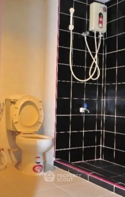 Modern bathroom with black tiled shower and white toilet, featuring a wall-mounted water heater.