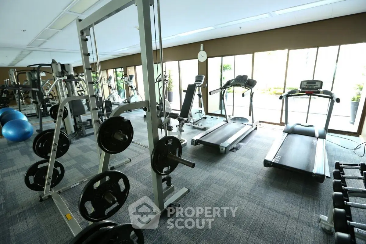 Spacious gym with modern equipment and large windows in luxury residential building.