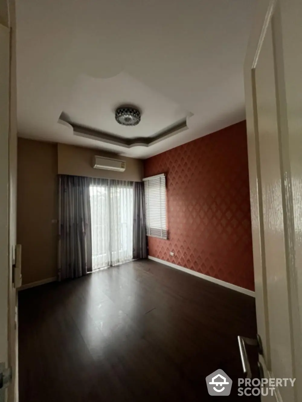 Spacious living room with elegant dark flooring, textured red accent wall, and sophisticated ceiling design, complemented by ample natural light.